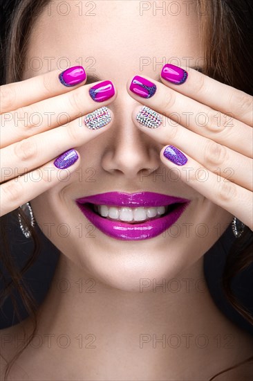 Beautiful girl with a bright evening make-up and purple manicure with rhinestones. Nail design. Beauty face. Picture taken in the studio on a black background