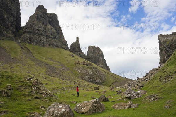 Hiker in red outdoor jacket in the bizarre rock world of Quiraing