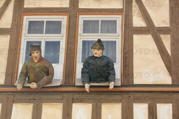 Two dolls figures looking out of the window of the house