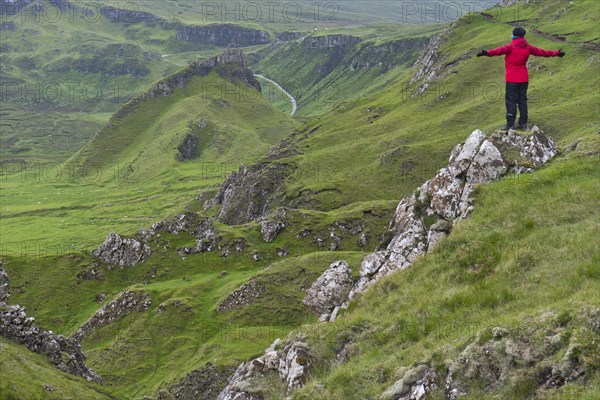 Hiker in red outdoor jacket in the bizarre rock world of Quiraing