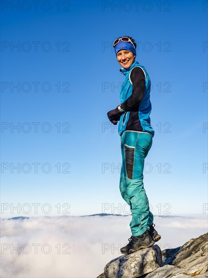 Mountaineer standing exposed on a rock above the clouds