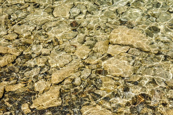 Sun casts fascinating play of light and shadow on the clear water and beige-brown stones on the shore of Lake Walen