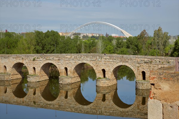 Roman stone arch bridge Puente Romano with reflection in the river Rio Guadiana and modern arch bridge Puente Lusitania