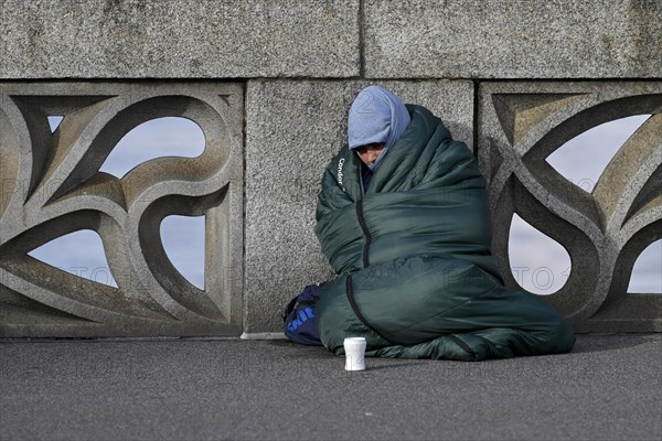 Homeless person with sleeping bag and cup