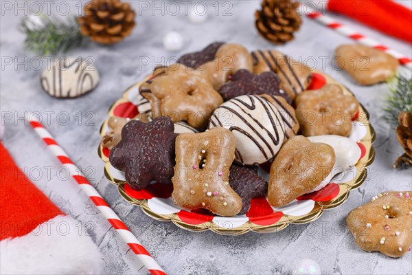 Traditional German gingerbread cookies with sugar and brown and white chocolate glazing in heart and star shape on striped plate surrounded by seasonal Christmas decoration