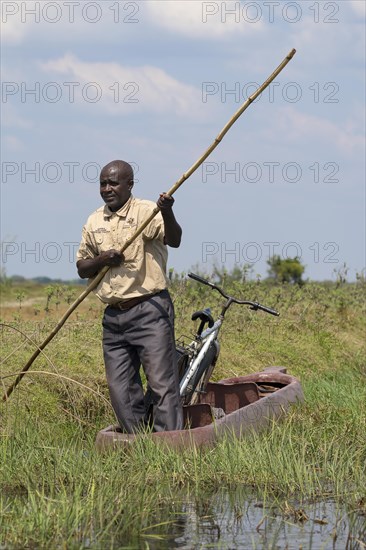 Man pushing dugout canoe with bicycle through swamp