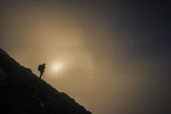 Mountaineer on mountain slope with fog against the light