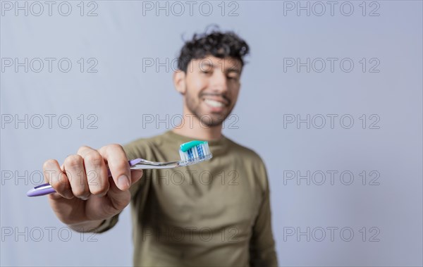 Smiling man showing a toothbrush in the foreground. Smiling young man showing toothbrush with toothpaste isolated. Smiling people holding toothbrush with toothpaste with copy space