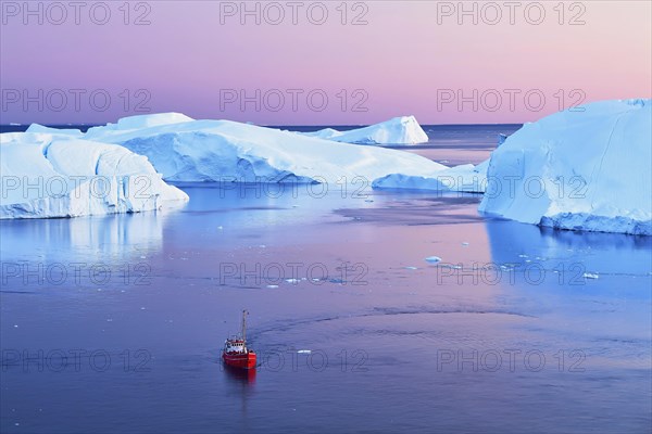 Red boat with tourists in front of icebergs at blue hour