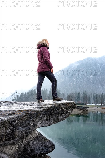 Woman standing on stone in front of foggy lake in winter with snow