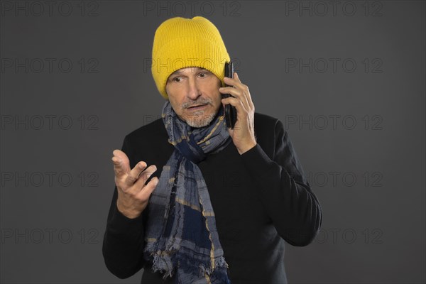 Elderly man with yellow winter cap excitedly talking on the phone