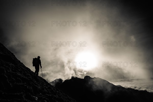 Mountaineer on mountain slope with fog against the light