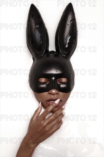 Beautiful african american woman with classic makeup in a milk bath wearing a black bunny mask. Beauty face