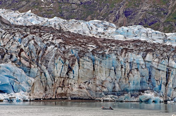 Small boat with two people in front of the huge front of a glacier