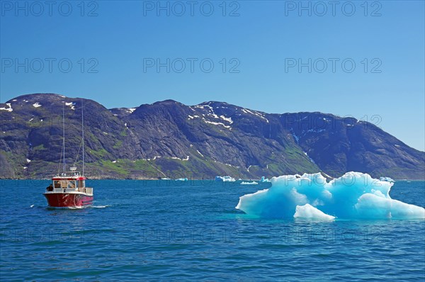 Piece of ice glistening in the sun next to a small passenger boat