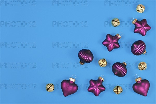 Christmas flat lay with purple tree ornament baubles and golden bells in corner of blue background with empty copy space