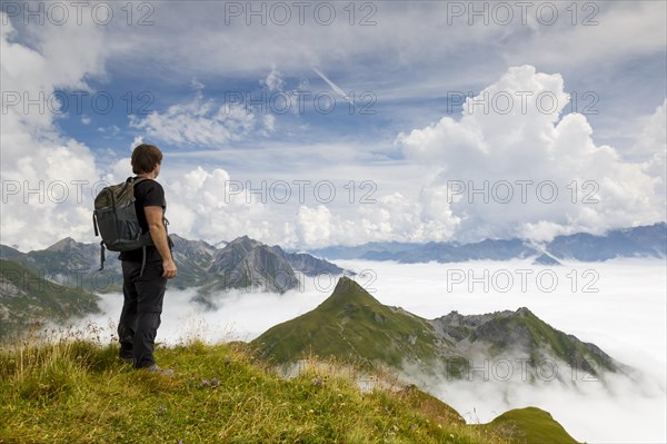 A hiker looks above the clouds at the peaks of the Alps on the Gehrengrat