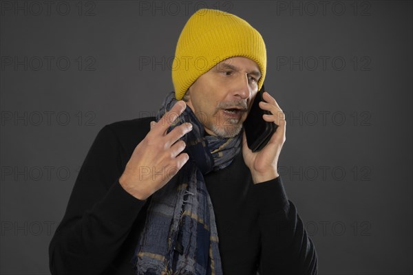 Elderly man with yellow winter cap excitedly talking on the phone