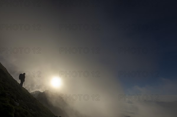 Mountaineer on mountain slope with fog against the light