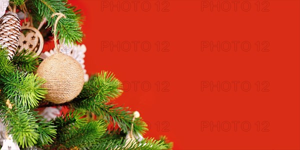 Banner with Christmas tree branches with natural ornament bauble made from beige jute rope on red background