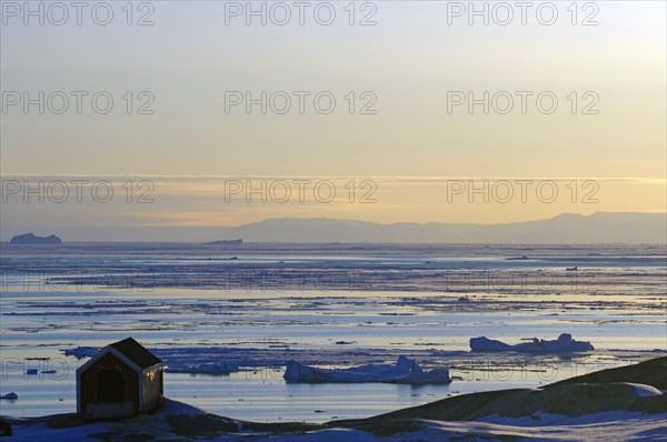 Doghouse standing on rocks in front of a bay littered with icebergs