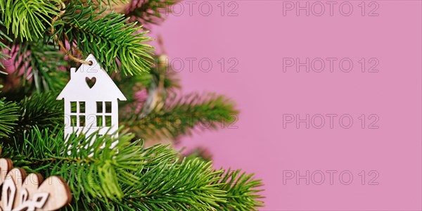 Banner with Christmas tree decorated with white house shaped tree ornament baubles on pink background with empty copy space