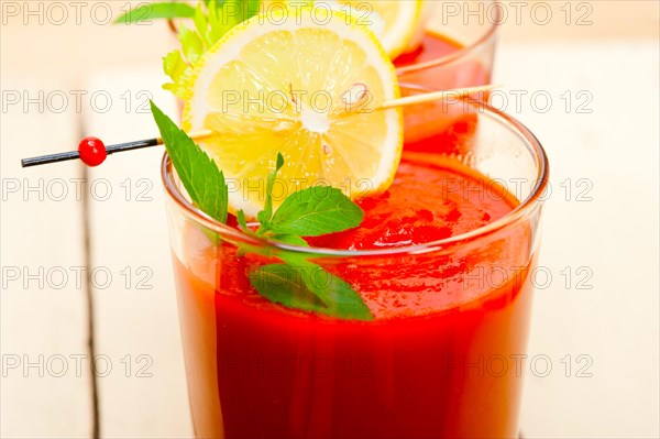 Fresh tomato juice gazpacho soup on a glass over white wood table