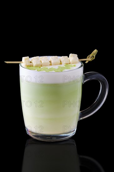 Matcha latte with pieces of coconut on skewer on black background