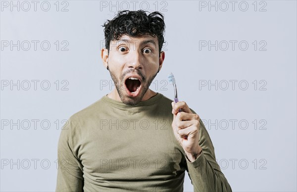 Surprised young man holding a toothbrush. Amazed teenager holding toothbrush isolated