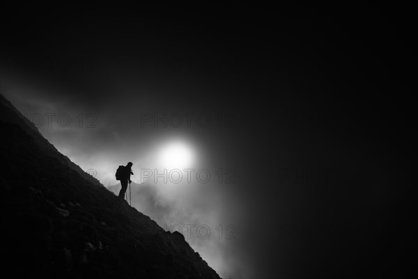 Mountaineer on mountain slope with fog against the light