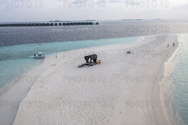 Aerial view: lonely sandbank in the Maldives with a table and sun loungers for romantic dinners