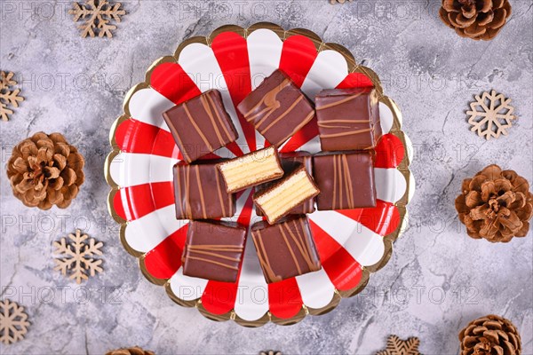 German layered winter cake pralines called Baumkuchen on striped plate next to seasonal pine cones and wooden snowflake ornaments