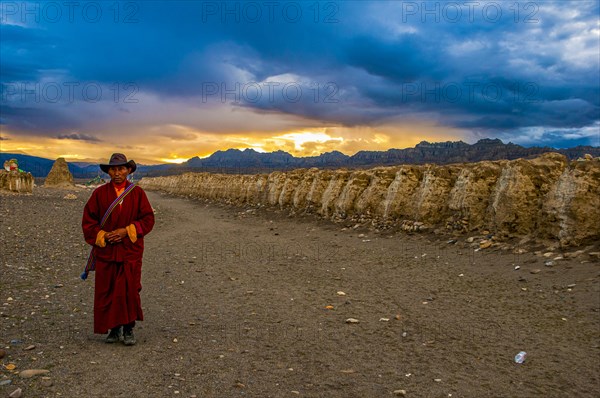 Monk walks along an eroded mud wall in the kingdom of Guge