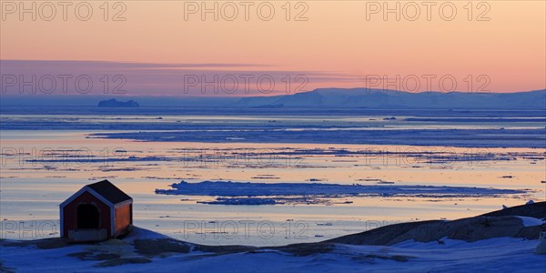 Doghouse in the evening light in front of a bay littered with icebergs