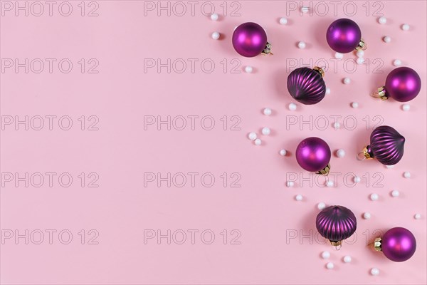 Seasonal purple Christmas tree bauble ornaments and white snowballs on side of light pink background with empty copy space