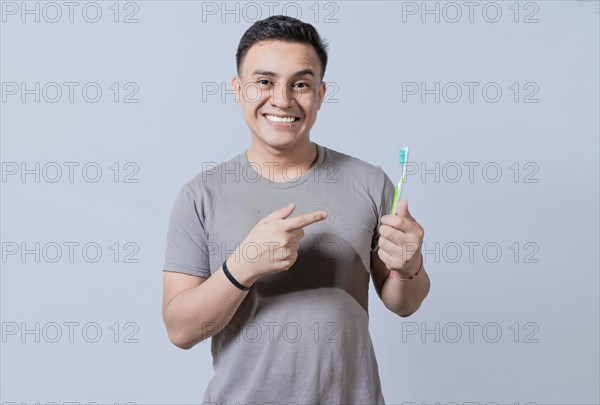 Handsome guy holding and pointing at toothbrush isolated. Person holding and pointing a toothbrush on isolated background