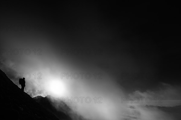 Mountaineer on mountain slope with fog against the light