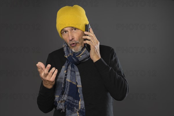 Elderly man with yellow winter cap excitedly talking on the phone