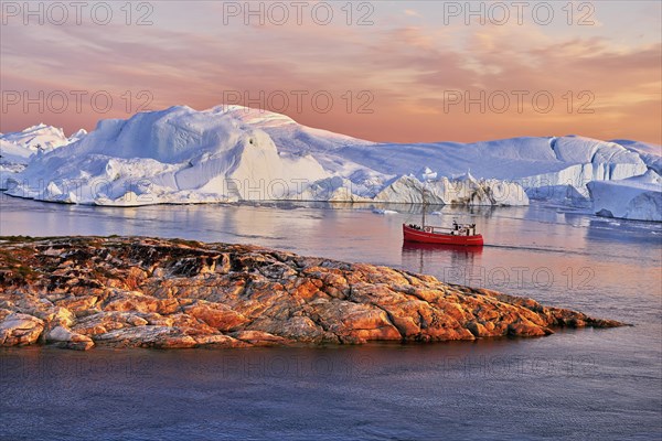 Red boat with tourists in front of icebergs in evening light
