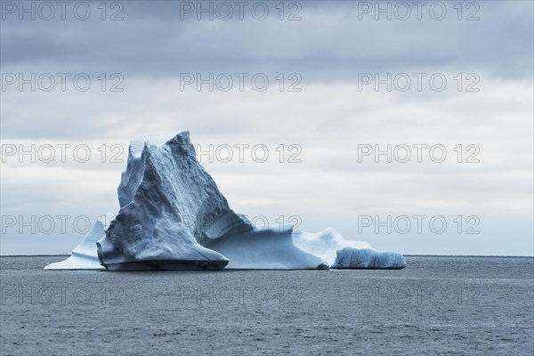 Iceberg drifting on the open sea against a dark cloudy sky