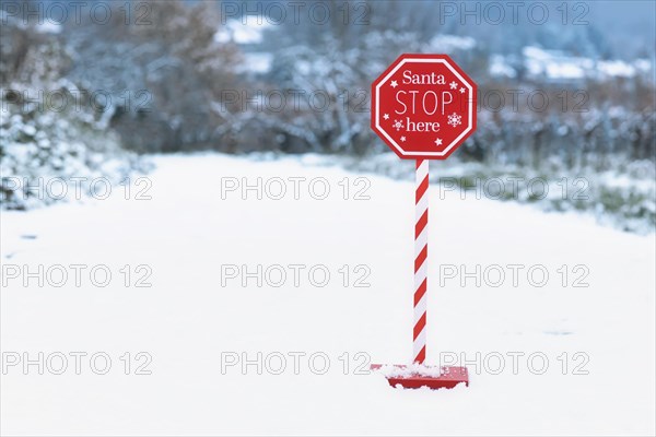 Red Christmas sign with text 'Santa Stop here' in snowy landscape