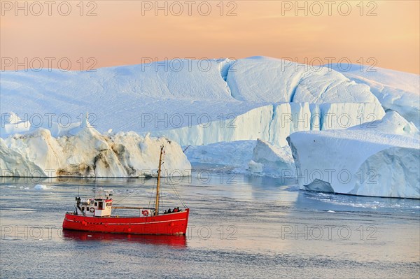 Red boat with tourists in front of icebergs in evening light