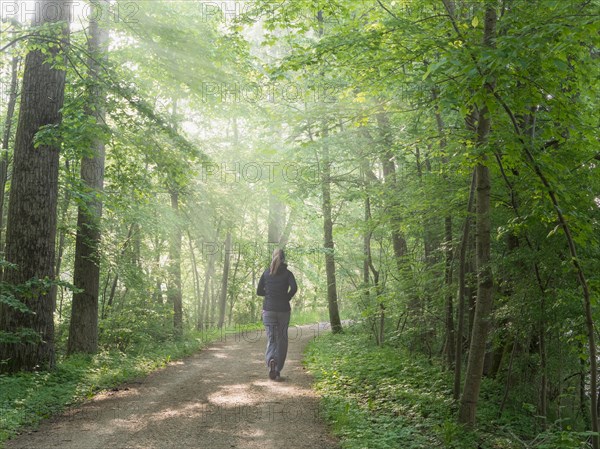 Young girl with long hair in grey clothes jogging in green forest