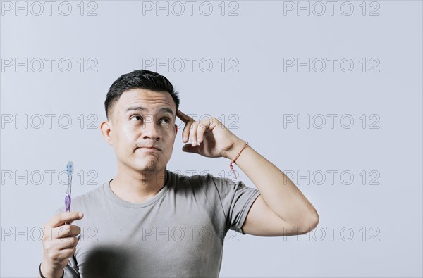 Man holding toothbrush with pensive expression isolated. Person holding toothbrush looking up