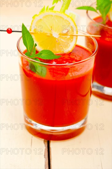 Fresh tomato juice gazpacho soup on a glass over white wood table