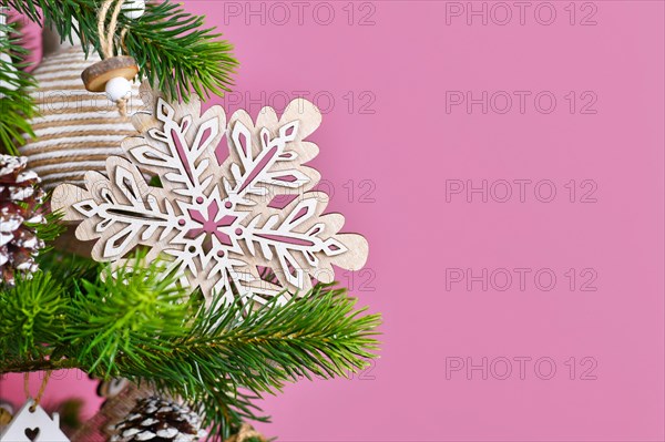 Christmas tree branch with natural wooden snowflake ornament in front of pink background with copy space