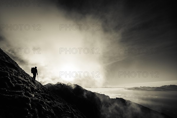 Mountaineer on mountain slope with fog against the light