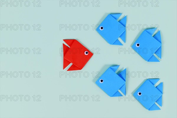 Paper fish swimming swimming against the current in other direction than different colored fish