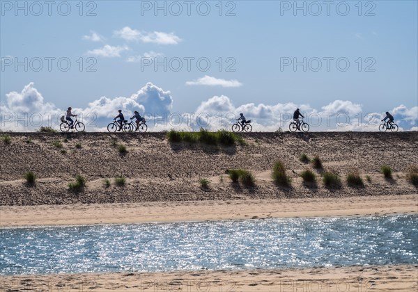 Silhouette of sporty people on bicycles outdoors against sun. Coast landscape with sand and water