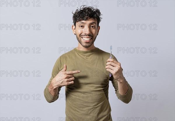 Smiling man holding and pointing at toothbrush. Handsome guy holding and pointing at toothbrush isolated. Person holding and pointing a toothbrush on isolated background